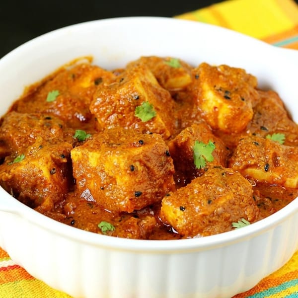 Spicy paneer curry in a white bowl, garnished with fresh cilantro and black seeds.